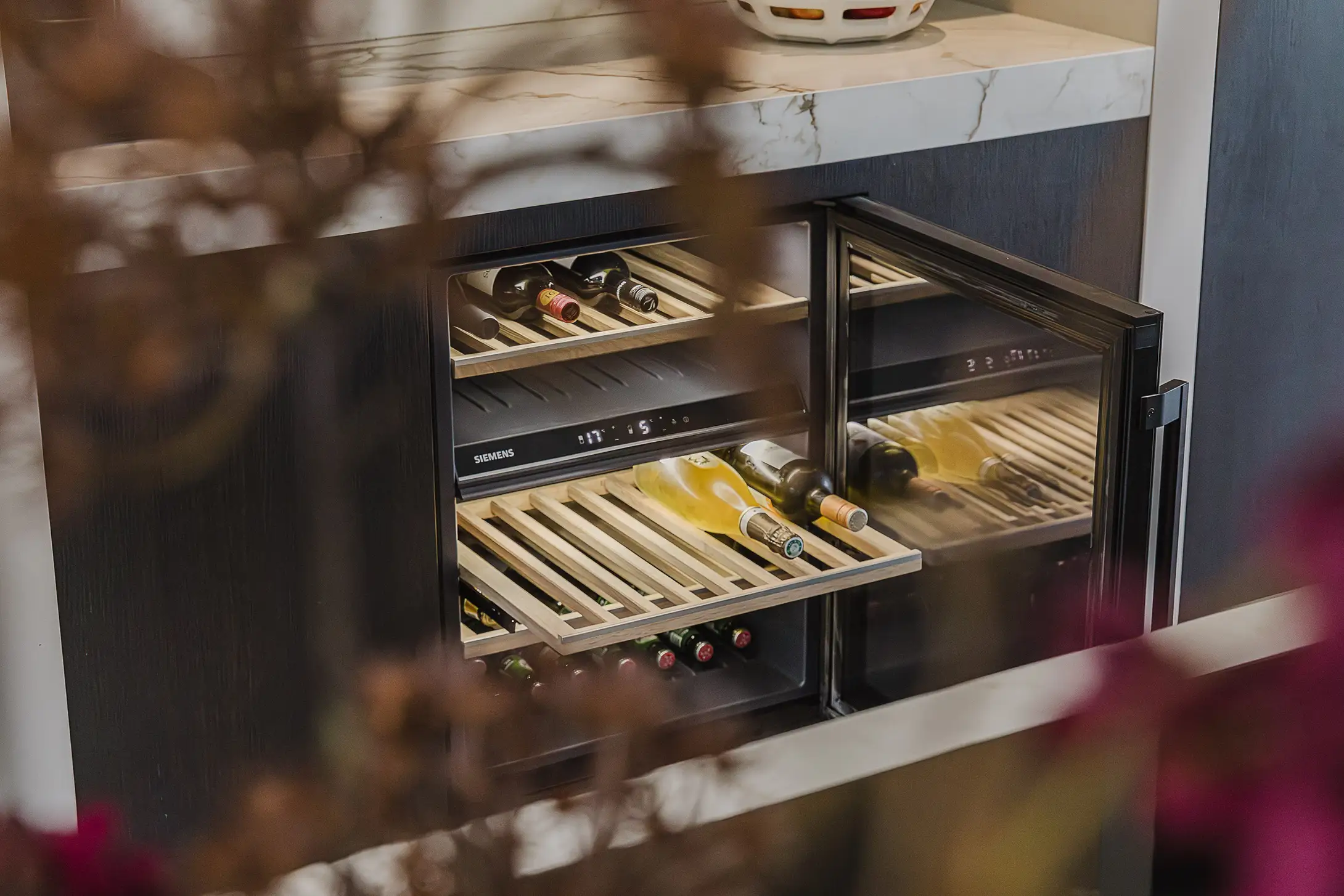 Geïntegreerde Siemens wijnkoelkast in de keuken met glazen deur open, flessen op houten uitschuifbare planken.