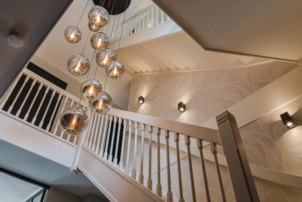 Wit geschilderd trappenhuis met klassieke balustrade en een grote cluster van moderne glazen bolvormige hanglampen.