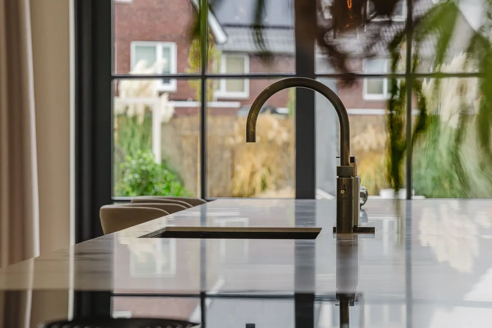 Close-up van een moderne, mat bronzen keukenkraan met hoge boog, staand op een glanzend donker keukeneiland.
